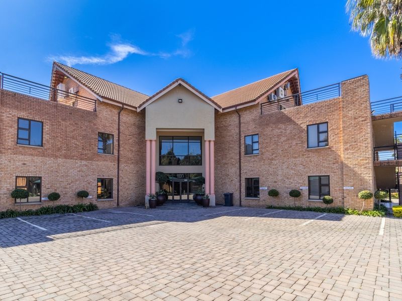 Front elevation of a multi-story brick office building featuring a paved parking area, glass entrance, and balcony access.