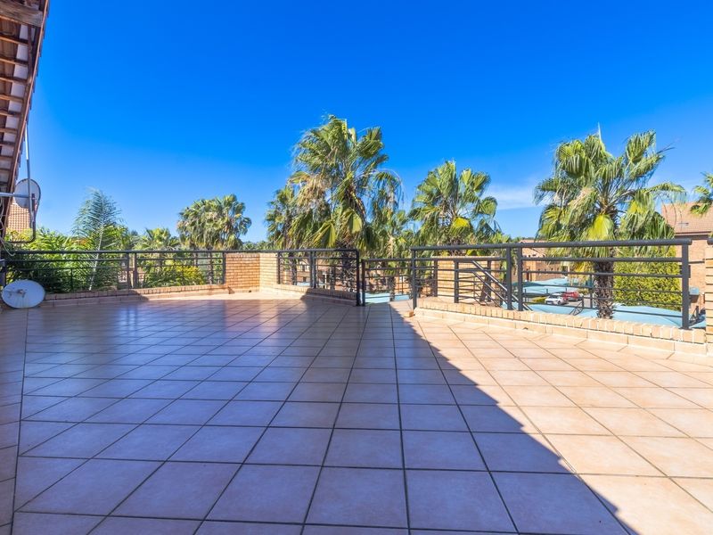 A spacious, open-air balcony featuring tiled flooring, a brick parapet wall, and metal railings, offering an elevated view of the surrounding landscape.