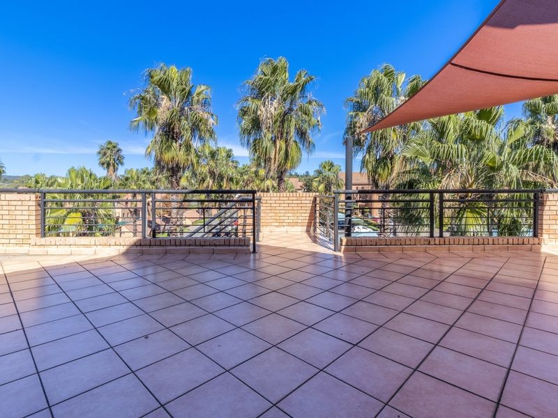 A spacious outdoor balcony featuring tiled flooring, a brick parapet wall with metal railings, and a shade sail, offering an open-air environment.