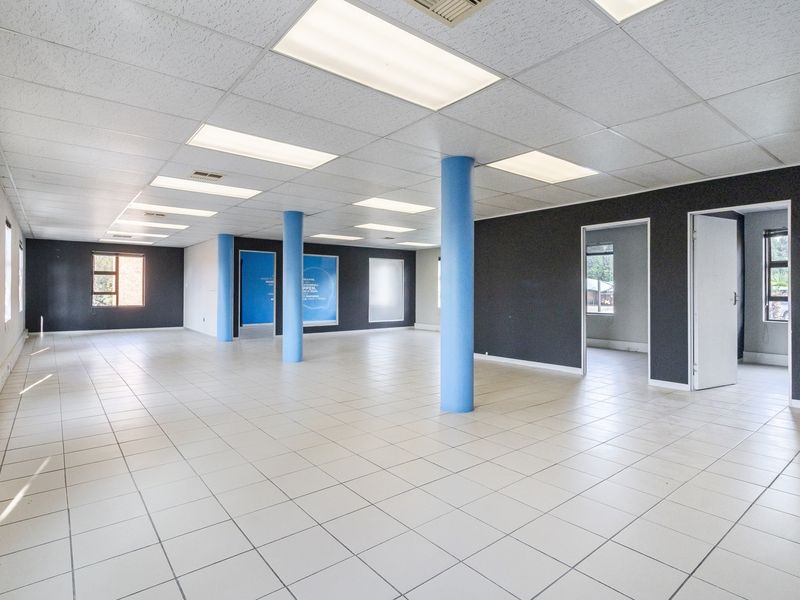 Spacious open-plan office area featuring a suspended ceiling with recessed lighting, ceramic tiled flooring, and structural support columns.