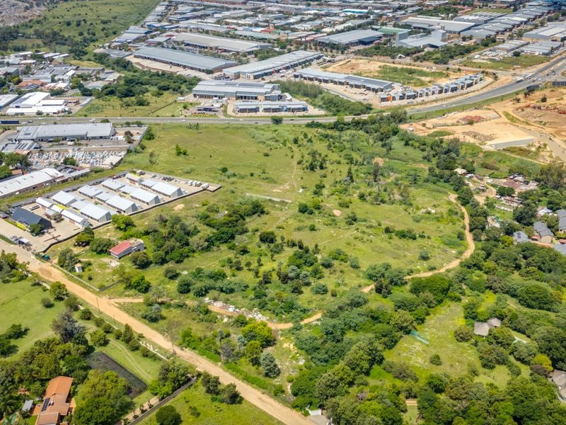 Aerial view of a large, undeveloped commercial land parcel featuring natural vegetation and dirt access roads, situated near established industrial and residential areas.