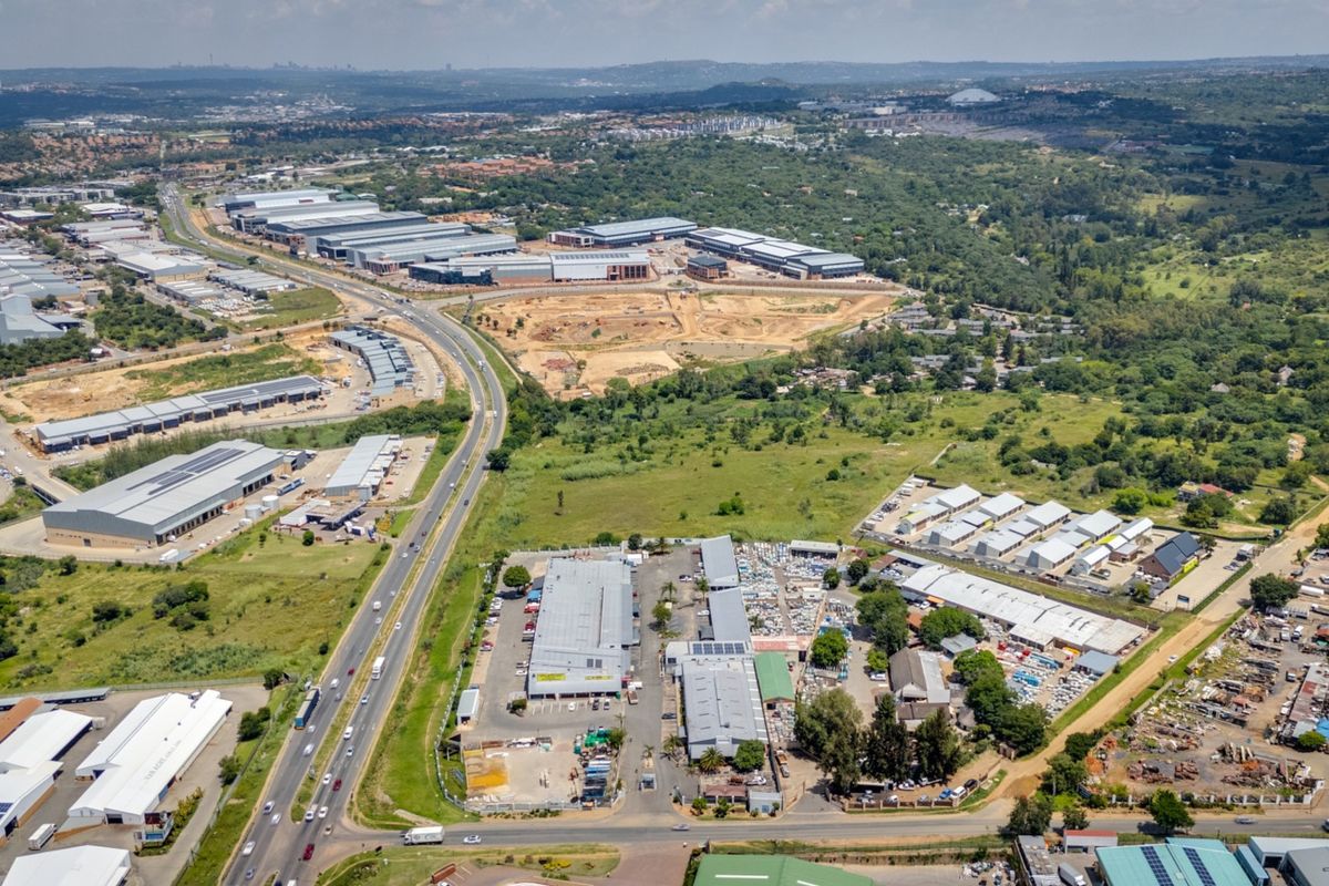 Aerial view of a commercial industrial park featuring multiple warehouse structures, paved access roads, and surrounding undeveloped land.