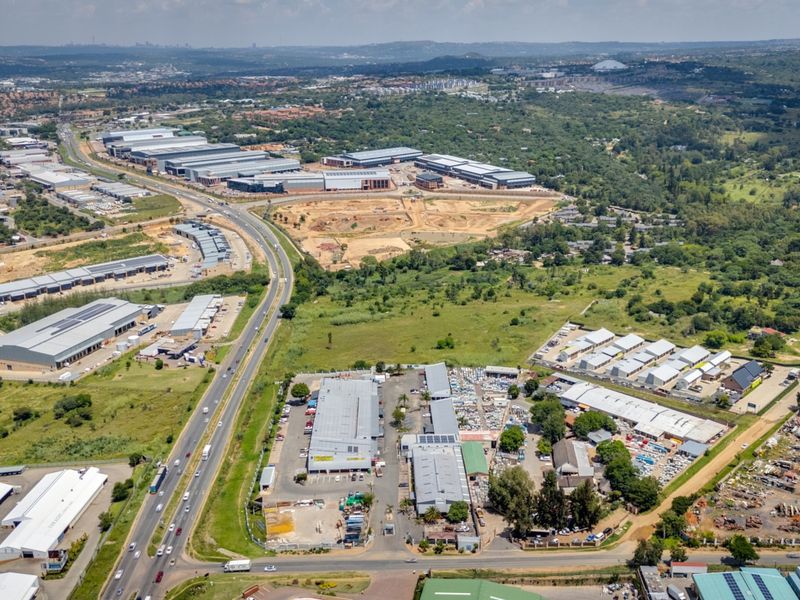 Aerial view of a commercial industrial park featuring multiple warehouse structures, paved access roads, and surrounding undeveloped land.