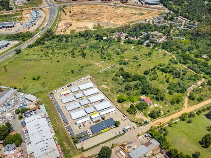 Aerial view of a commercial property featuring multiple storage units, paved access, and surrounding undeveloped land.