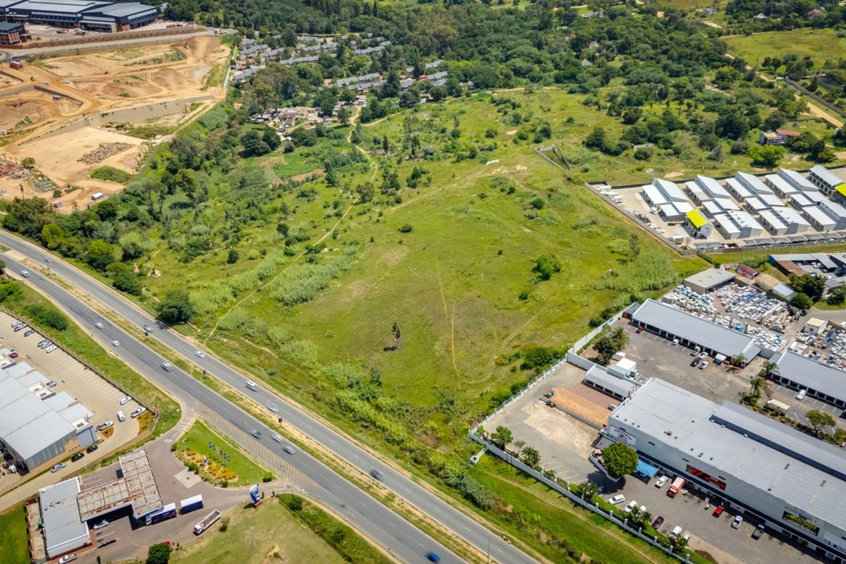 An aerial view of a large, undeveloped commercial land parcel situated near existing industrial and commercial developments with direct road access.