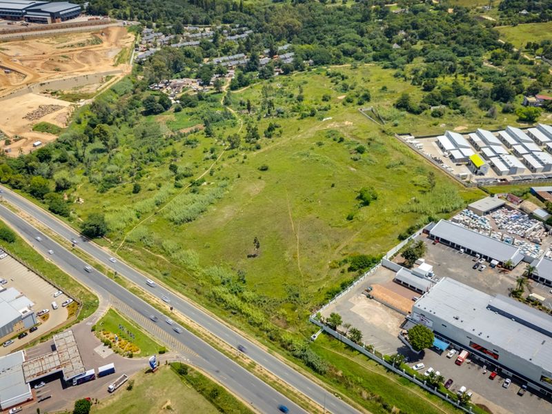 An aerial view of a large, undeveloped commercial land parcel situated near existing industrial and commercial developments with direct road access.