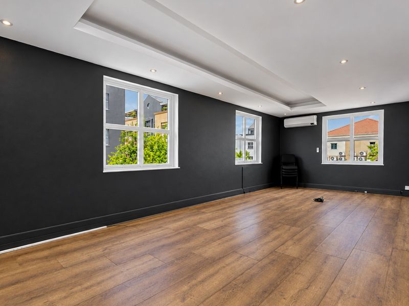 A spacious, modern office area featuring dark accent walls, wood-look laminate flooring, recessed ceiling lighting, and a wall-mounted air conditioning unit.