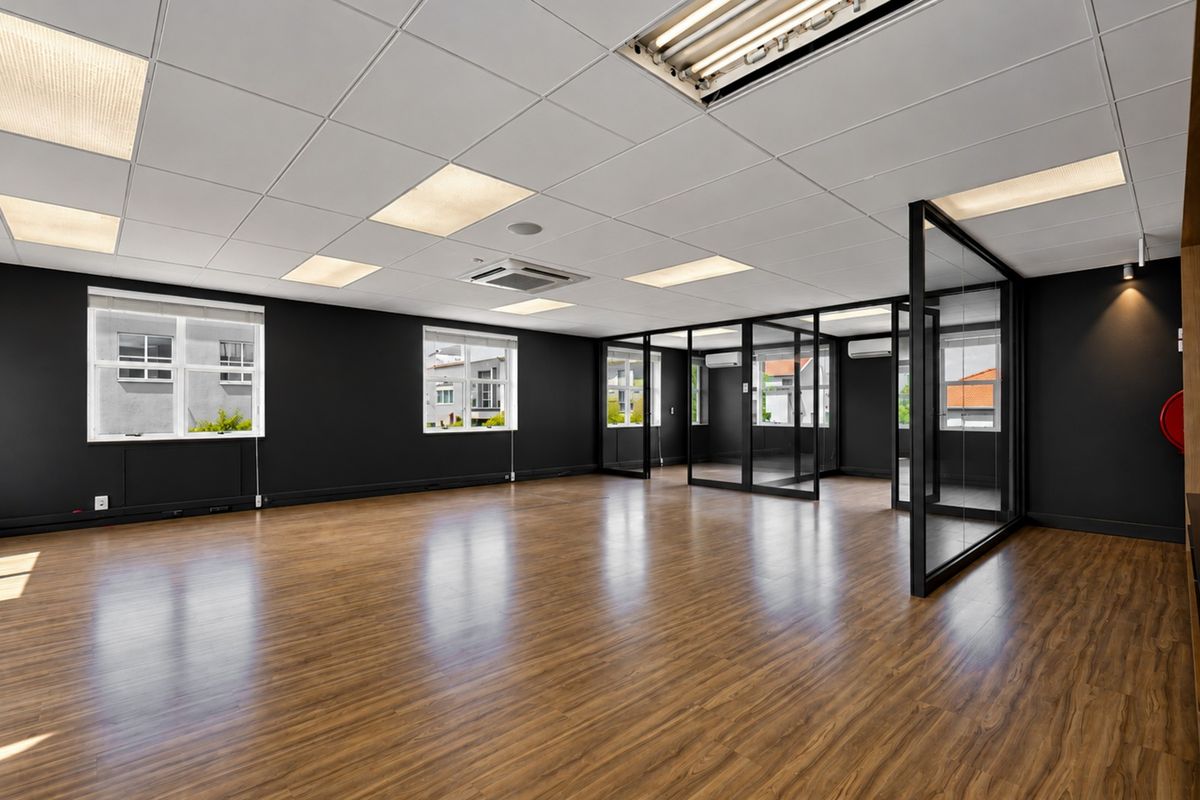 A modern, open-plan office space featuring laminate flooring, a suspended ceiling with recessed lighting, and sleek glass partition walls.