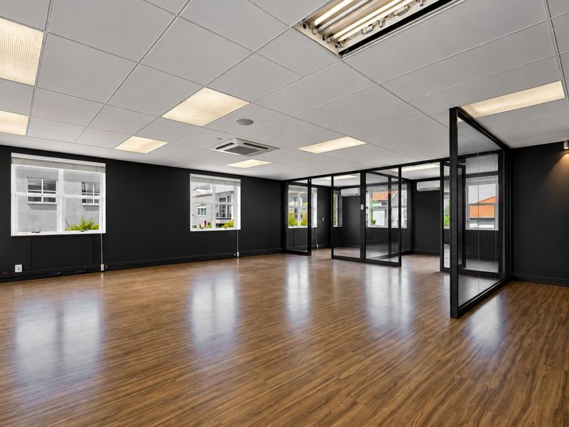 A modern, open-plan office space featuring laminate flooring, a suspended ceiling with recessed lighting, and sleek glass partition walls.