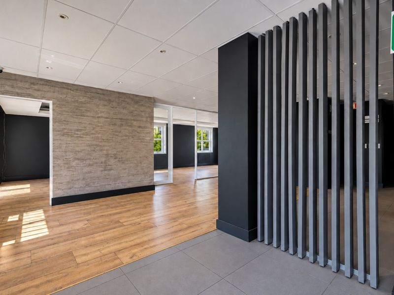 Modern open-plan office space featuring a mix of timber-look and tiled flooring, glass partitions, and a decorative timber slat feature wall.