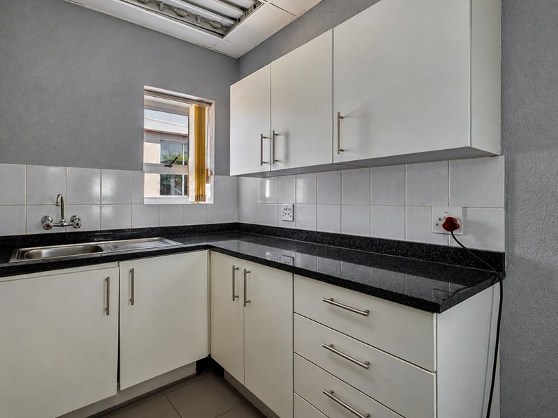 A compact office kitchenette featuring white built-in cabinetry, dark granite countertops, a stainless steel sink, and tiled backsplash.