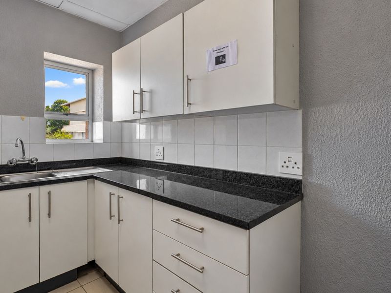 A clean, functional office kitchenette featuring white cabinetry, dark granite countertops, a stainless steel sink, and tiled backsplash.