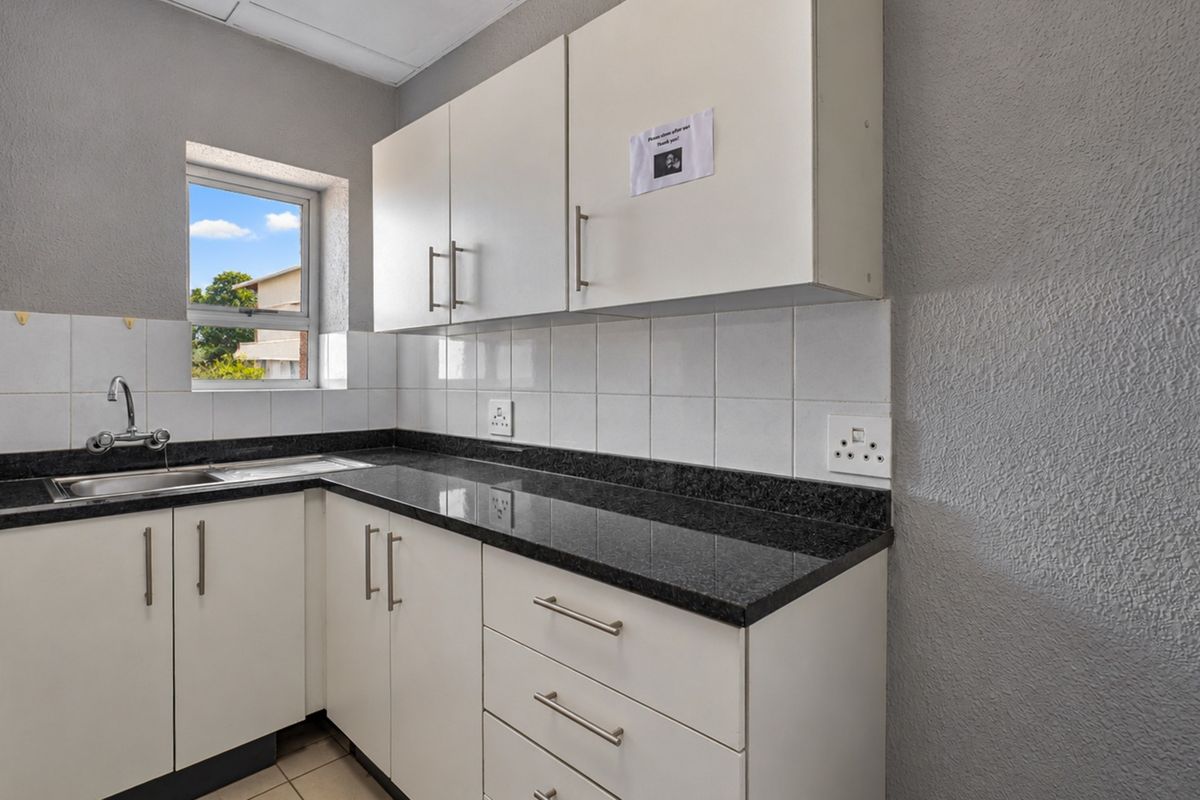 A clean, functional office kitchenette featuring white cabinetry, dark granite countertops, a stainless steel sink, and tiled backsplash.