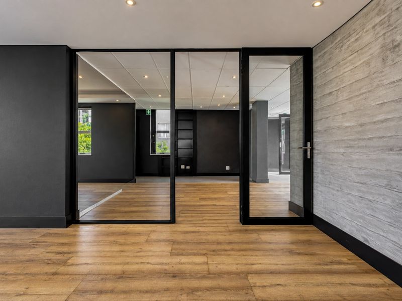 Modern office space featuring laminate flooring, a textured concrete accent wall, and a sleek black-framed glass partition providing an open, professional atmosphere.