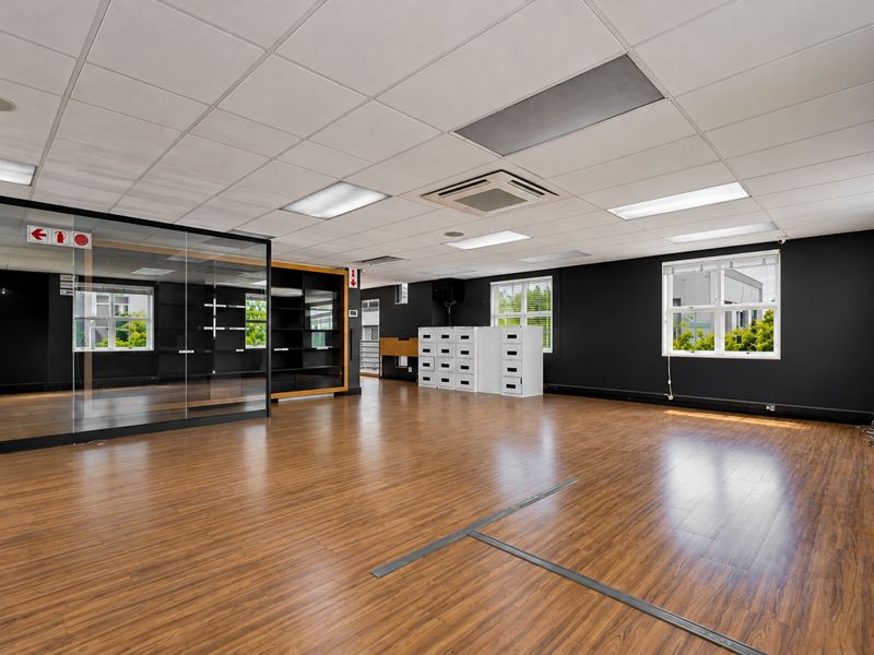 Spacious open-plan office area featuring laminate flooring, a suspended ceiling with recessed lighting, integrated air conditioning, and a modern glass-partitioned meeting room.
