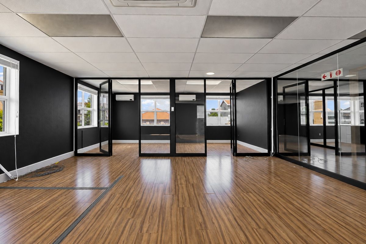 Modern open-plan office space featuring laminate flooring, glass partitions, suspended ceilings, and integrated split-system air conditioning units.