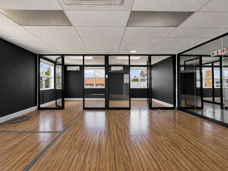 Modern open-plan office space featuring laminate flooring, glass partitions, suspended ceilings, and integrated split-system air conditioning units.