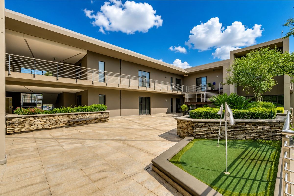 A well-maintained office courtyard featuring stone retaining walls, a small putting green, and modern multi-level building facades with stainless steel balustrades.