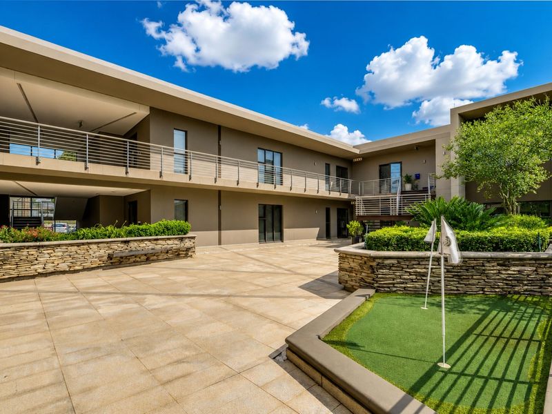 A well-maintained office courtyard featuring stone retaining walls, a small putting green, and modern multi-level building facades with stainless steel balustrades.