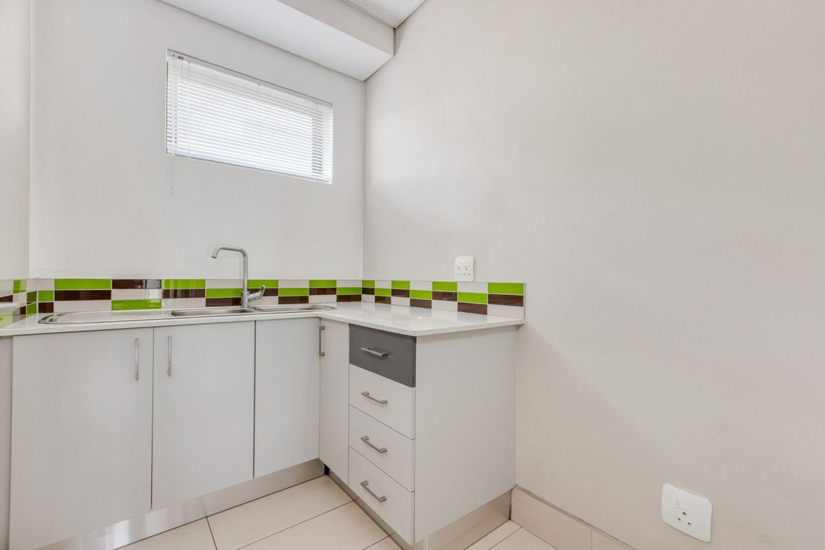 A clean, compact kitchenette featuring modern white cabinetry, a stainless steel sink, and a decorative tiled backsplash in an office environment.