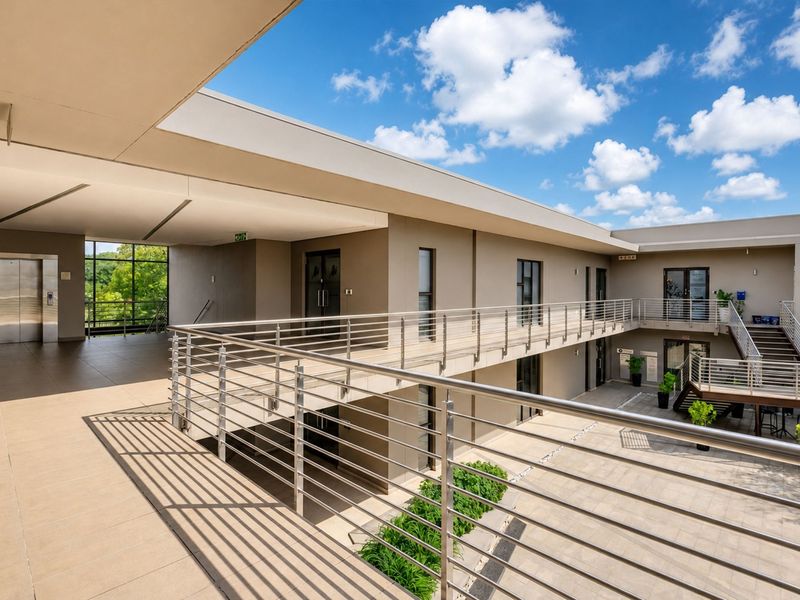 Modern office building exterior featuring a multi-level courtyard, stainless steel railings, tiled walkways, and integrated elevator access.