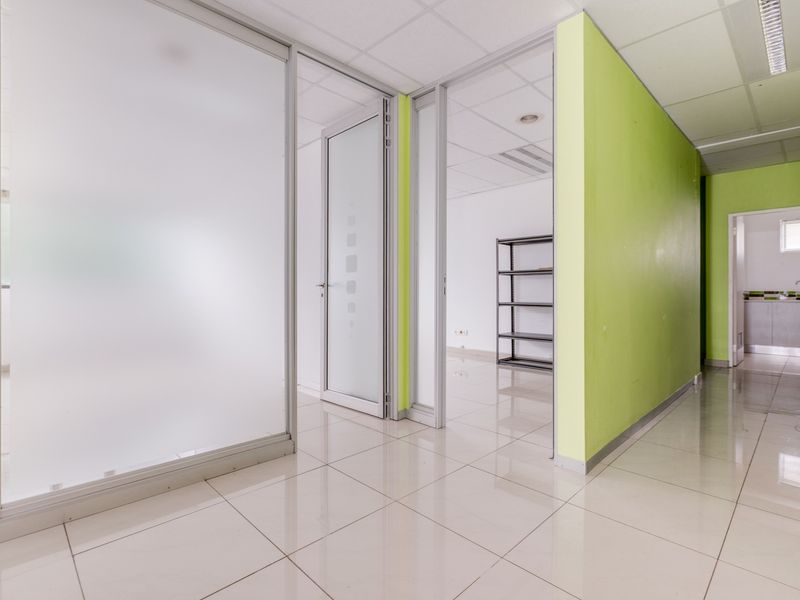 Modern office space featuring frosted glass partitions, tiled flooring, and a suspended ceiling, offering a clean and professional layout.