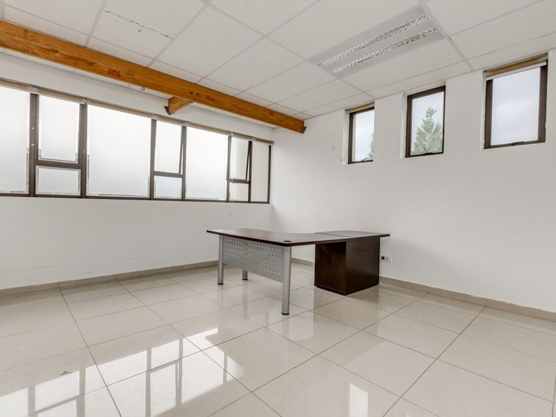 A bright office space featuring tiled flooring, a suspended ceiling with recessed lighting, and large windows providing ample natural light.