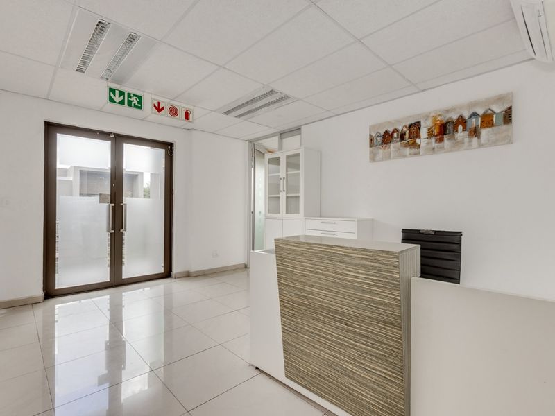 A bright and professional office reception area featuring tiled floors, a modern reception desk, glass entrance doors, and a suspended ceiling with recessed lighting.