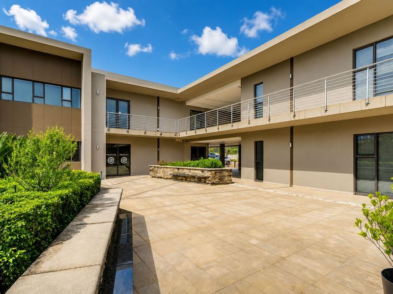 A well-maintained modern office courtyard featuring tiled flooring, a stone-clad planter box, and a second-story balcony with stainless steel balustrades.