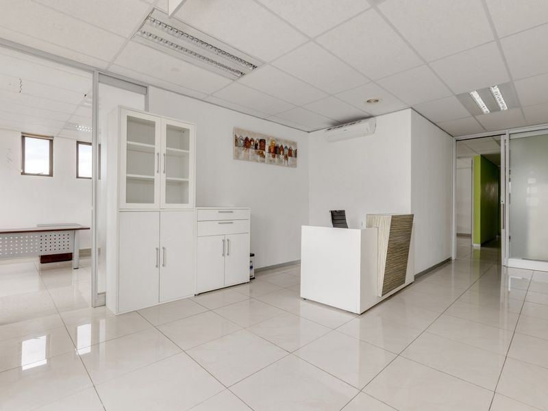 Modern office reception area featuring tiled flooring, suspended ceilings with recessed lighting, and glass partition walls leading to adjacent workspaces.