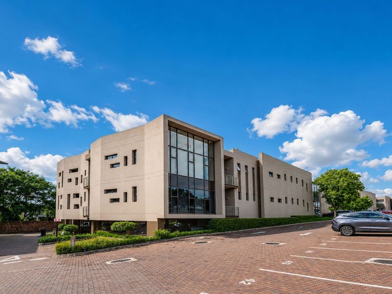 Modern multi-story office building exterior featuring a prominent glass facade, paved parking area, and well-maintained landscaped surroundings.