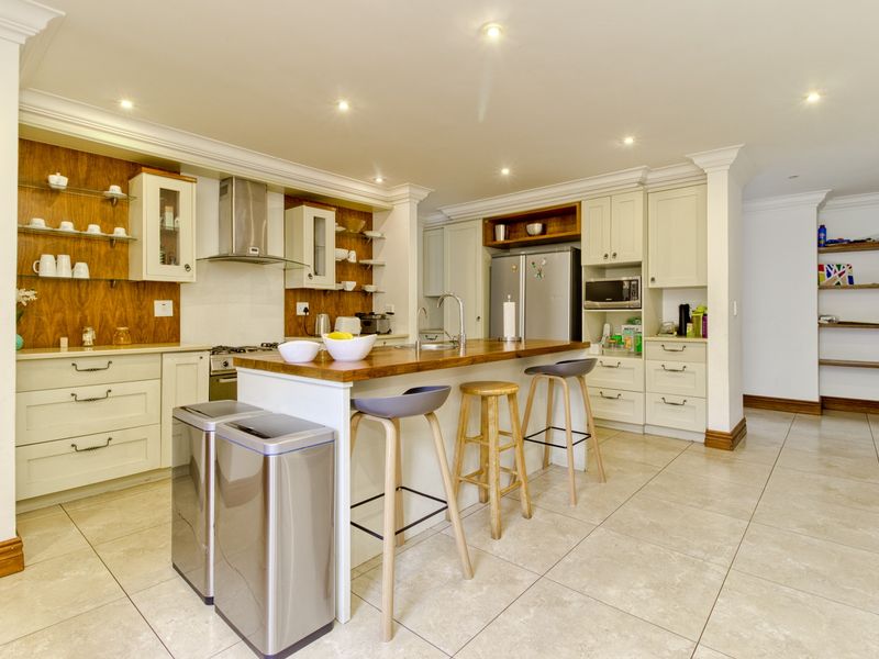 Modern kitchen featuring a central island with a wooden countertop, ample built-in cabinetry, integrated appliances, and tiled flooring with recessed lighting.
