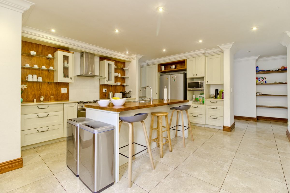 Modern kitchen featuring a central island with a wooden countertop, ample built-in cabinetry, integrated appliances, and tiled flooring with recessed lighting.
