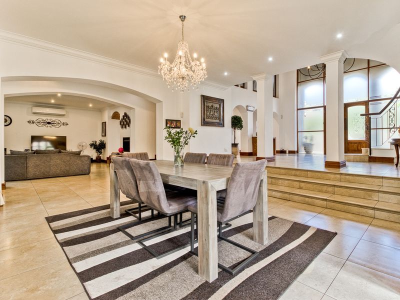 Spacious open-plan dining and living area featuring tiled floors, elegant arched architectural details, a grand chandelier, and a staircase leading to the upper level.
