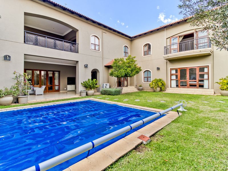 Spacious rear exterior featuring a swimming pool with cover, a covered patio area, and upper-level balconies overlooking a well-maintained garden.