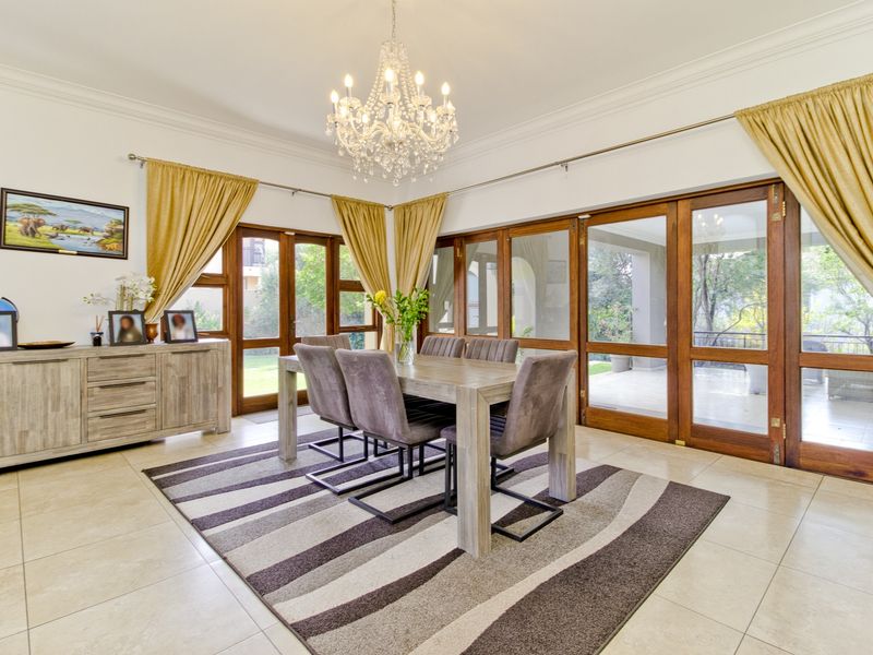 Spacious dining room featuring elegant tiled flooring, a crystal chandelier, and large wooden-framed glass doors providing access to the patio.