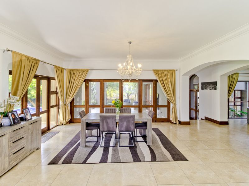 Spacious dining room featuring tiled flooring, elegant crystal chandelier, and large wooden-framed glass doors providing natural light and access to the outdoor area.