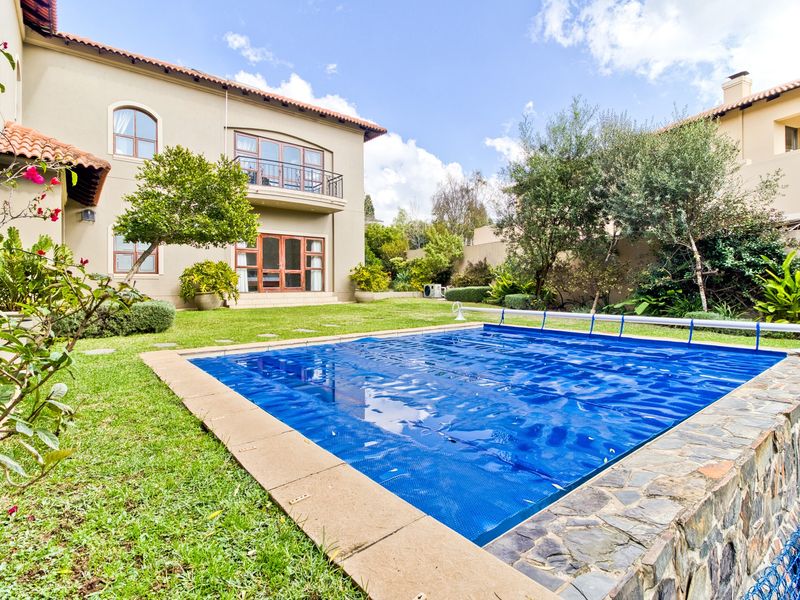 A well-maintained rear garden featuring a swimming pool with a cover, stone retaining wall, and a two-story residence with a balcony.
