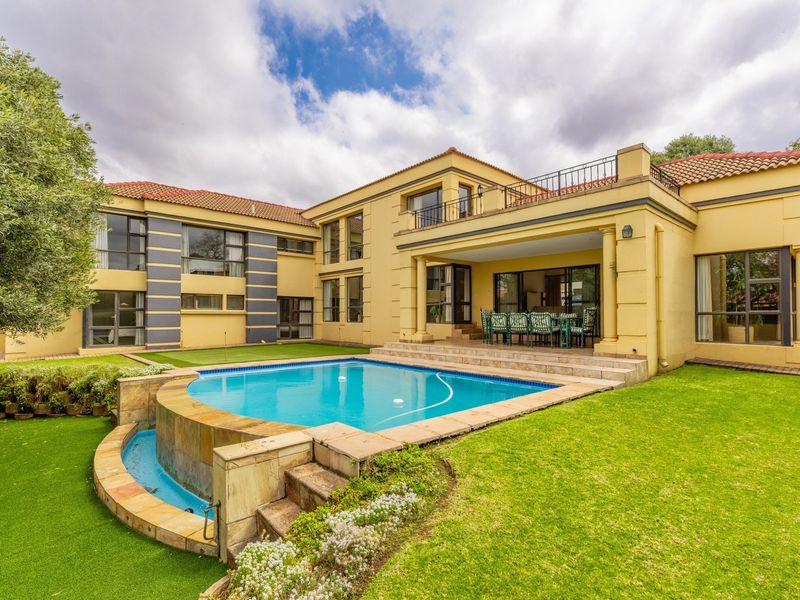 Spacious rear exterior featuring a swimming pool with stone surround, covered patio, upper-level balcony, and well-maintained landscaped garden.