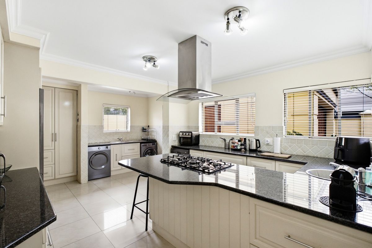 Spacious kitchen featuring granite countertops, a central island with a gas hob, stainless steel extractor fan, and integrated laundry facilities.