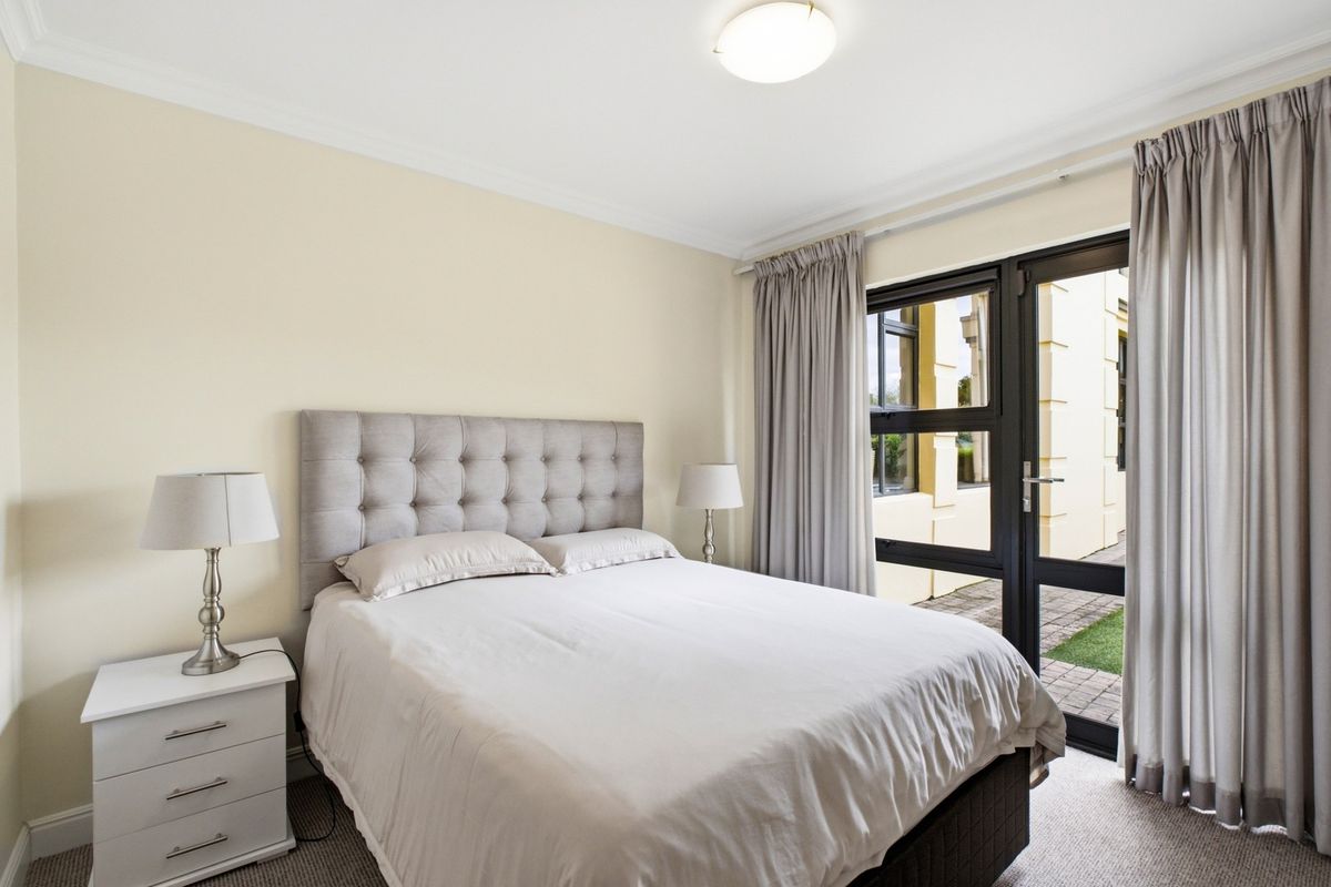 A well-maintained bedroom featuring neutral walls, carpeted flooring, and direct access to an outdoor area through glass-paned french doors.