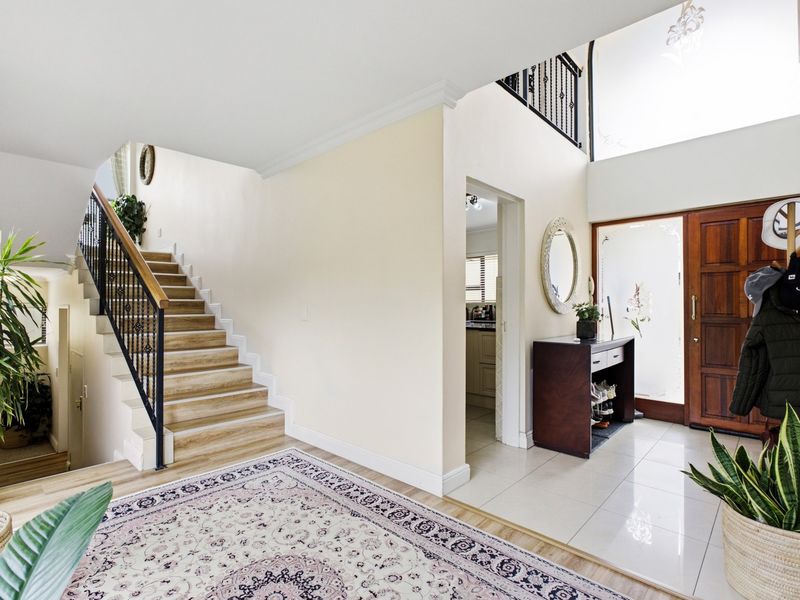 Spacious entrance hall featuring a grand staircase with wrought iron balustrade, tiled flooring, and a solid timber front door with frosted glass sidelight.