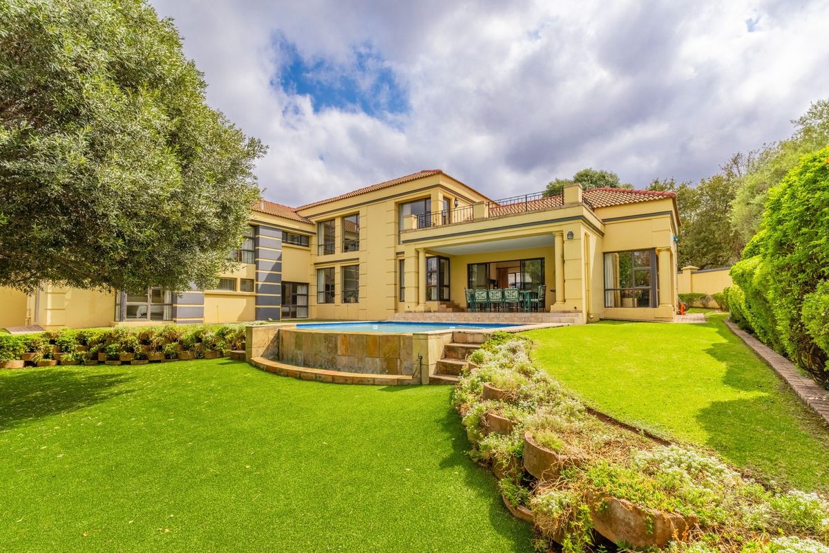 Spacious rear exterior view featuring a well-maintained garden, a raised swimming pool with stone cladding, and a covered patio area.