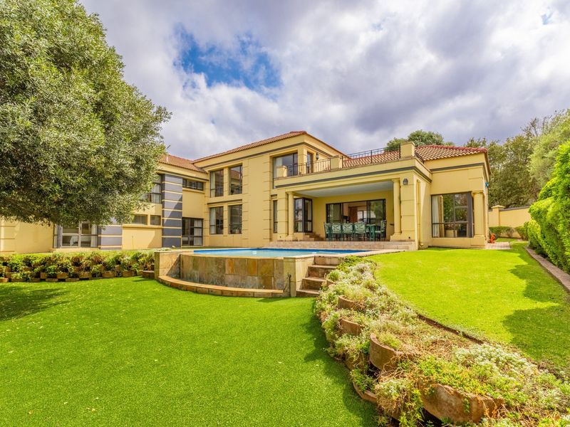 Spacious rear exterior view featuring a well-maintained garden, a raised swimming pool with stone cladding, and a covered patio area.