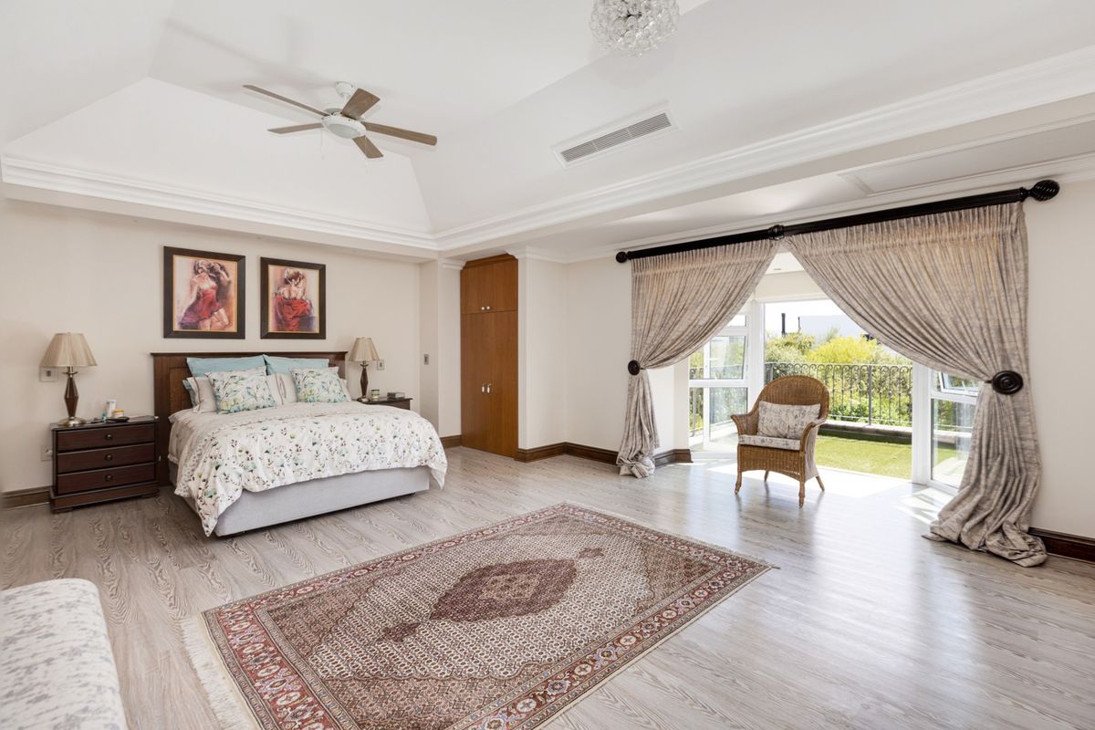 Spacious bedroom featuring high vaulted ceilings, wood-look flooring, built-in cabinetry, and direct access to a private balcony through large glass sliding doors.