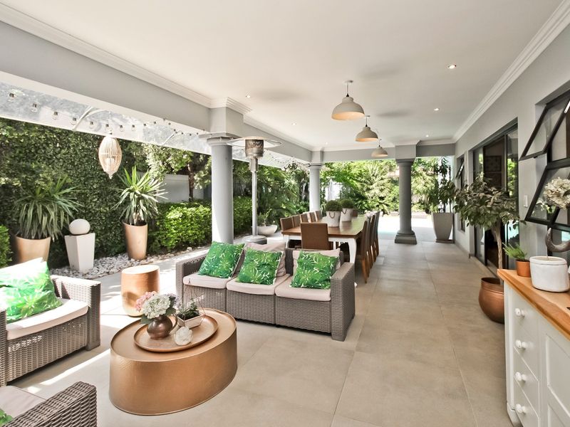 Spacious covered patio featuring large format floor tiles, recessed lighting, and structural columns, providing a seamless transition to the garden area.
