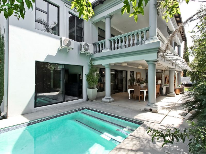 A well-maintained outdoor area featuring a swimming pool, a spacious covered patio with classic columns, and direct access to the home via sliding doors.