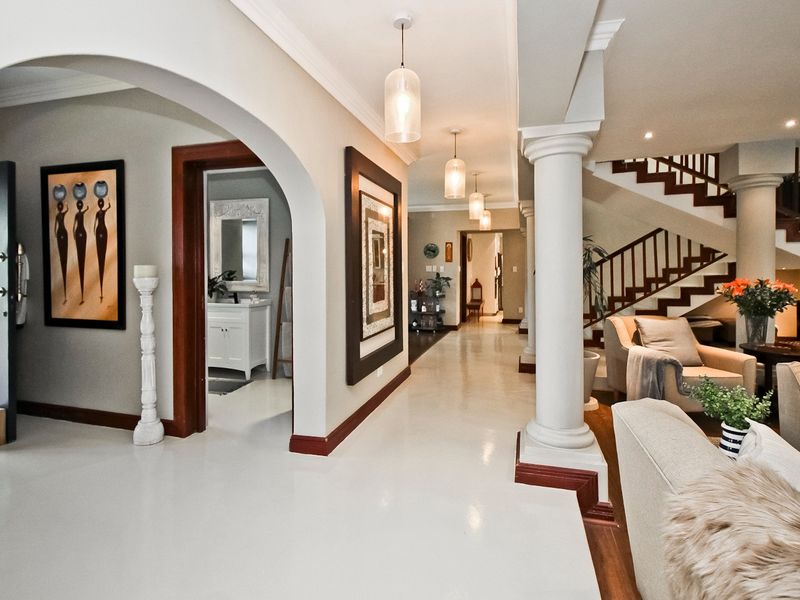 Spacious hallway featuring elegant arched doorways, classical columns, and a grand staircase with a wooden balustrade, leading into the main living areas.