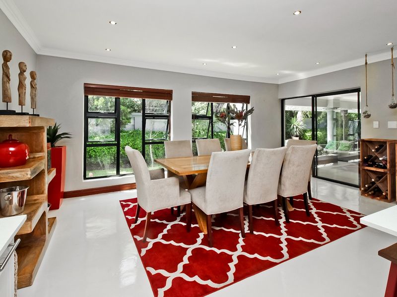 A bright and modern dining room featuring polished concrete floors, recessed lighting, and large aluminium-framed windows and sliding doors leading to the garden.