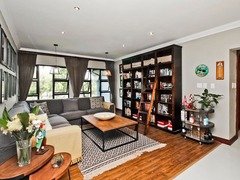 A well-maintained living room featuring timber flooring, recessed downlights, and a large built-in library shelving unit with an integrated sliding ladder.